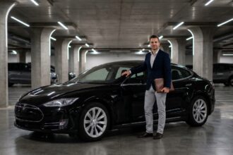 Homme en costume à côté d'une voiture de luxe noire dans un parking haut de gamme, illustrant l'assurance auto premium